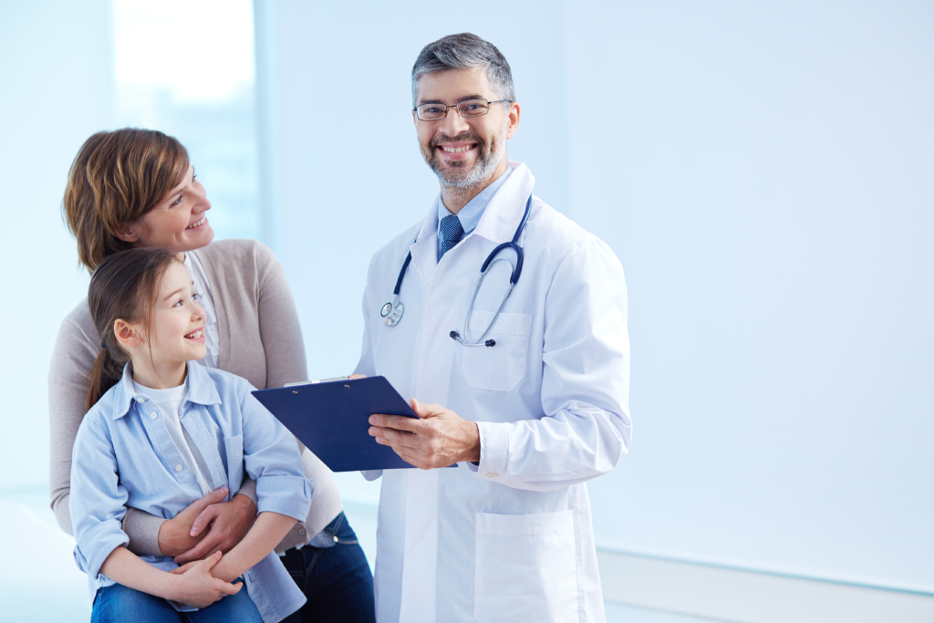 Profession libérale médicale en blouse blanche souriant avec une mère et sa fille dans un cabinet médical.